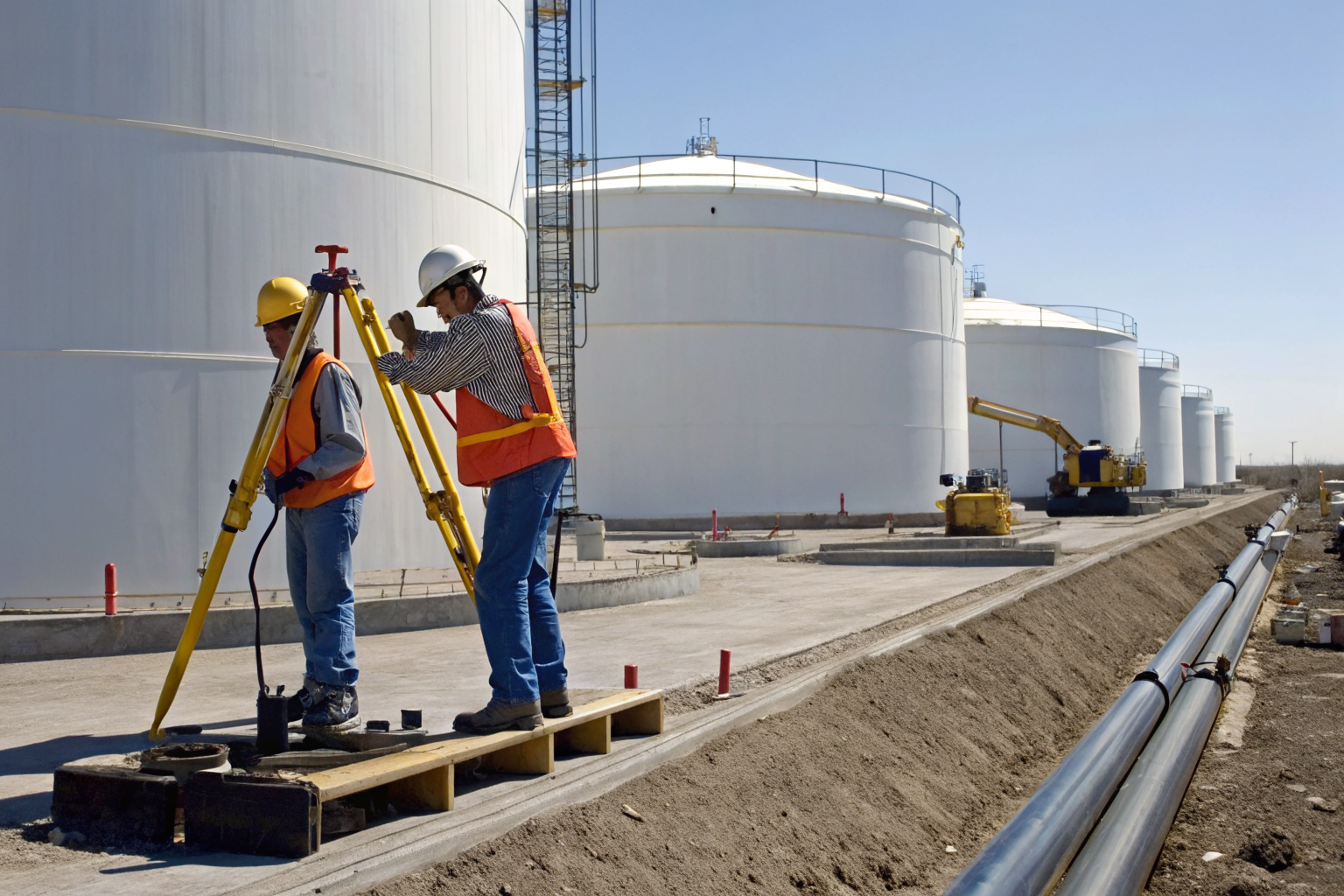 Workers building containment systems around oil tanks.