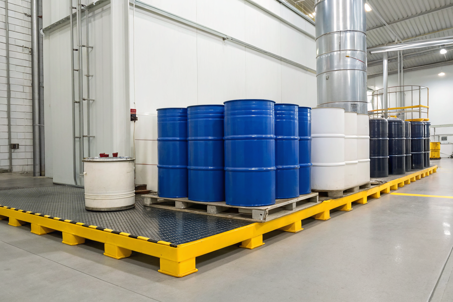 Chemical drums on a spill pallet in an industrial setting.